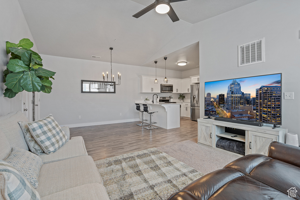 Living area featuring a chandelier, lofted ceiling, light wood-style floors, and ceiling fan
