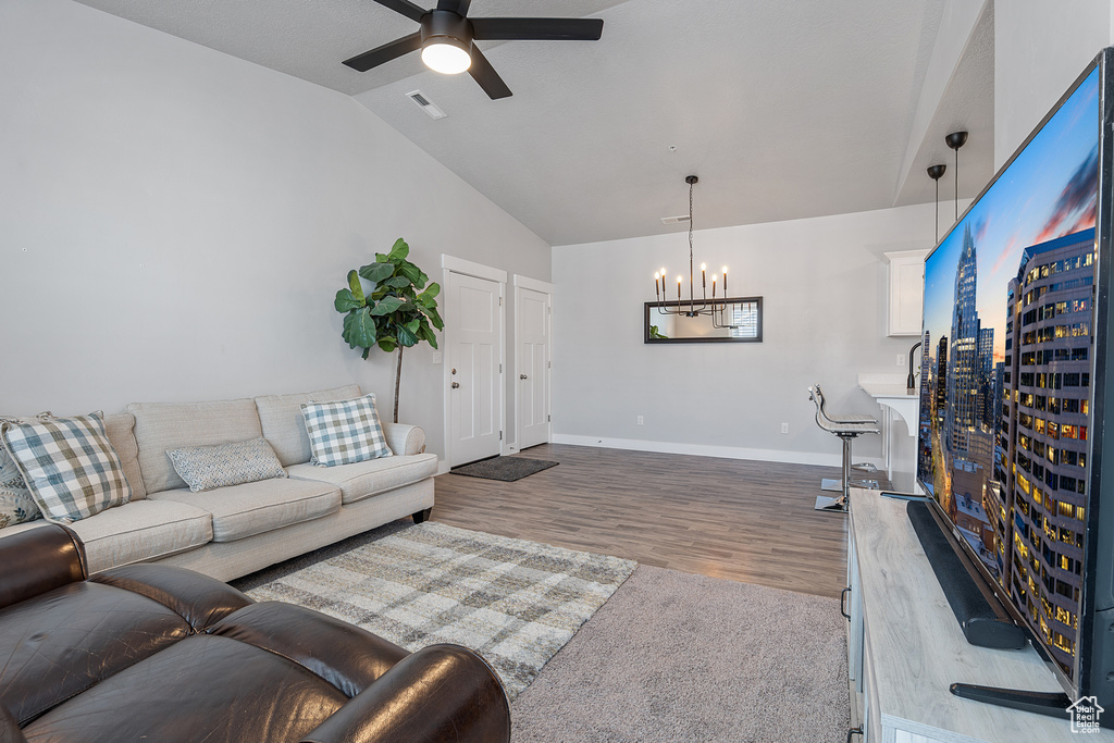 Living room with a chandelier, vaulted ceiling, wood finished floors, and ceiling fan