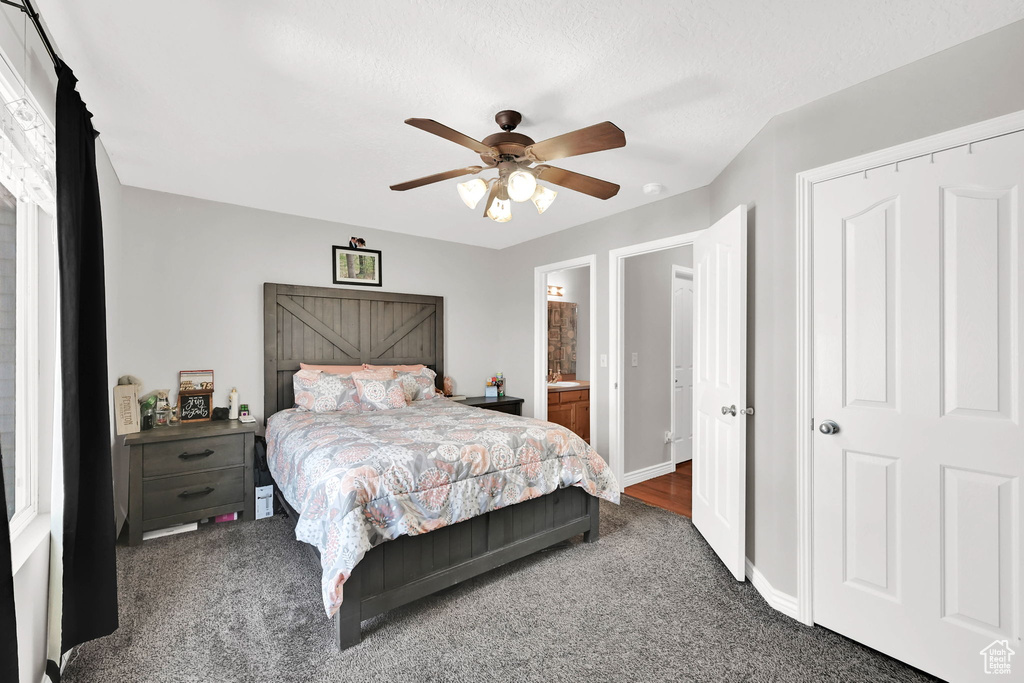 Bedroom with dark carpet, ceiling fan, and ensuite bath