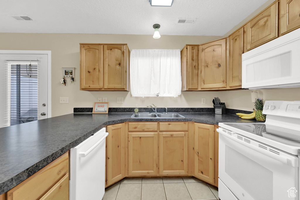 Kitchen with white appliances, light brown cabinetry, and light tile patterned flooring