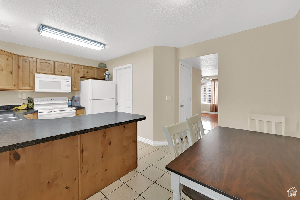 Kitchen with white appliances, a peninsula, light tile patterned floors, a textured ceiling, and dark countertops