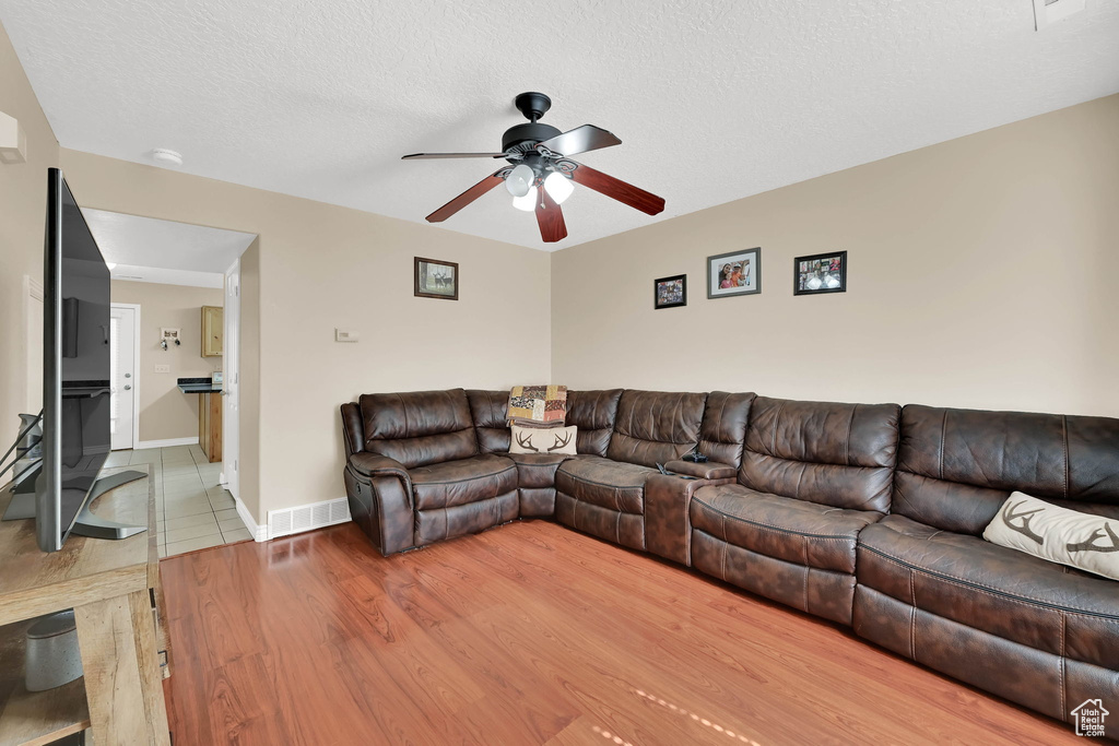 Living room with a ceiling fan, wood finished floors, and a textured ceiling