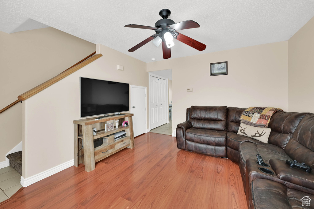 Living room featuring stairs, ceiling fan, wood finished floors, and a textured ceiling