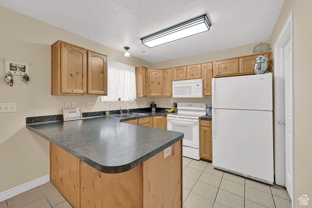 Kitchen featuring white appliances, a peninsula, dark countertops, light tile patterned floors, and a textured ceiling