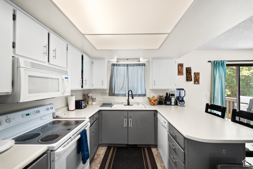 Kitchen with white appliances, a peninsula, gray cabinetry, light countertops, and white cabinets