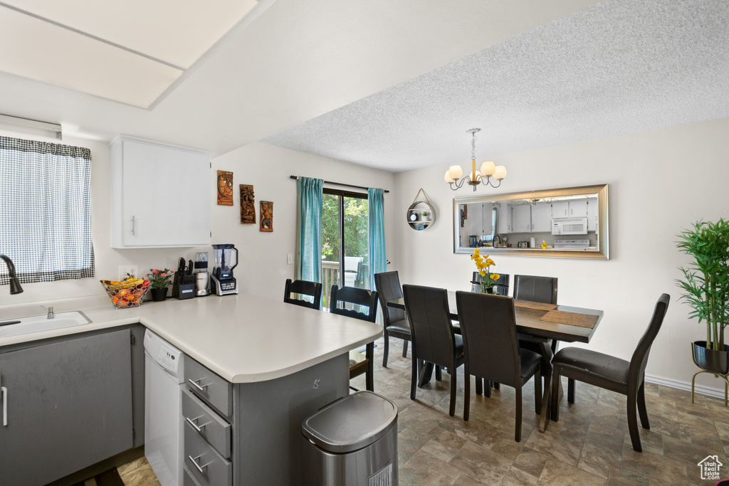 Kitchen featuring white appliances, a peninsula, gray cabinets, light countertops, and a chandelier