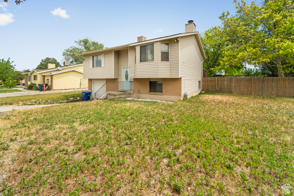 Raised ranch featuring a chimney, an attached garage, and brick siding