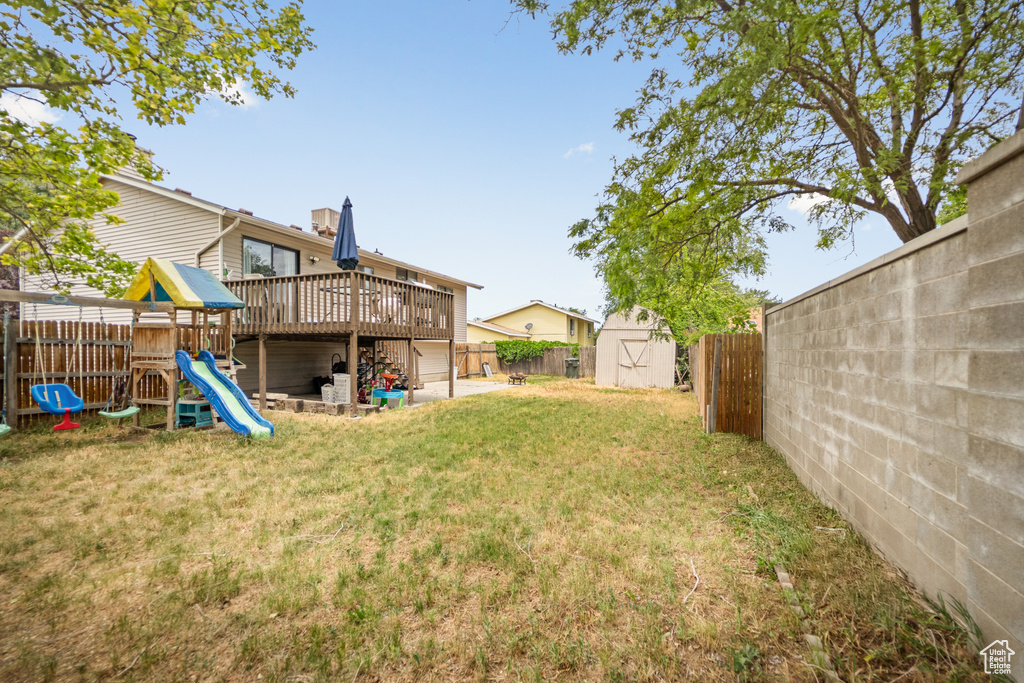 Fenced backyard featuring a shed, a playground, and a deck