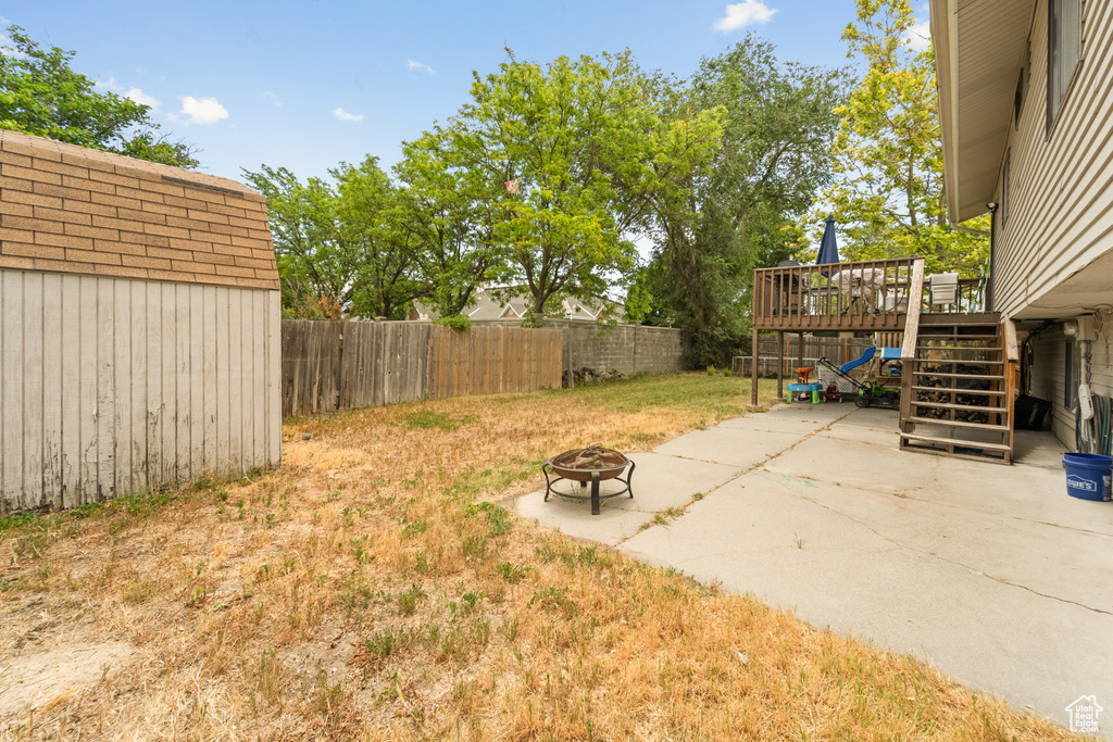 Fenced backyard featuring a fire pit, stairway, a patio, a wooden deck, and a shed