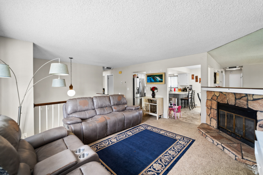 Carpeted living area featuring a textured ceiling and a stone fireplace