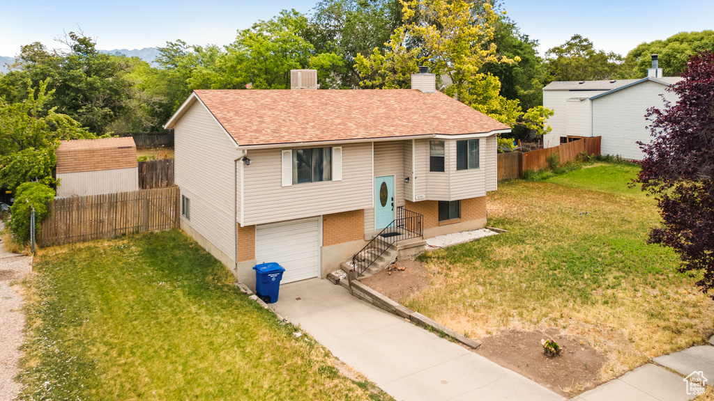 Bi-level home featuring driveway, a garage, a chimney, brick siding, and a shingled roof