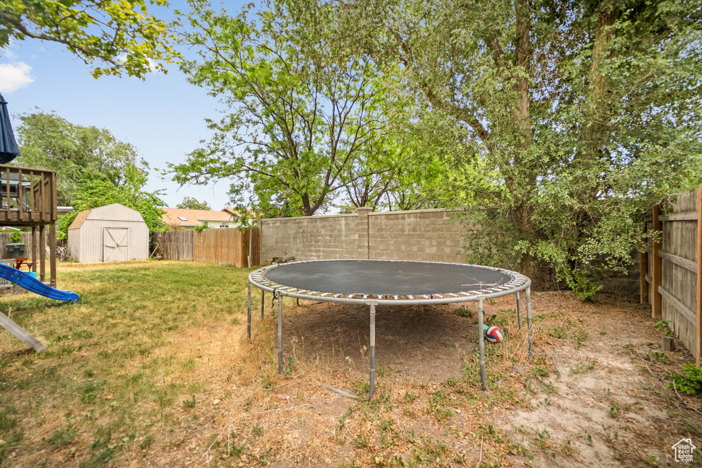 Fenced backyard featuring a trampoline and a shed