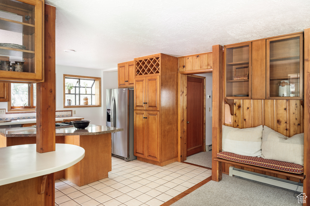 Kitchen featuring stainless steel fridge, baseboard heating, glass insert cabinets, a kitchen bar, and brown cabinets