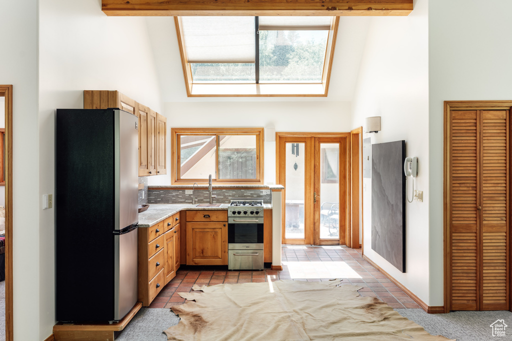 Kitchen with stainless steel appliances, a high ceiling, a skylight, light stone countertops, and light tile patterned floors