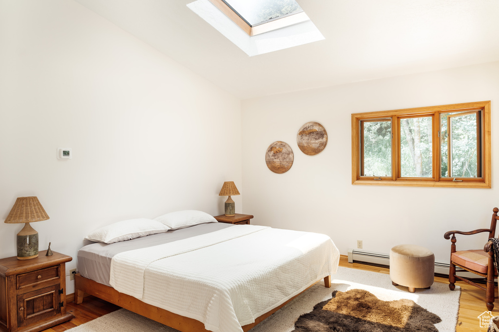 Bedroom featuring light wood-type flooring, a skylight, and a baseboard radiator