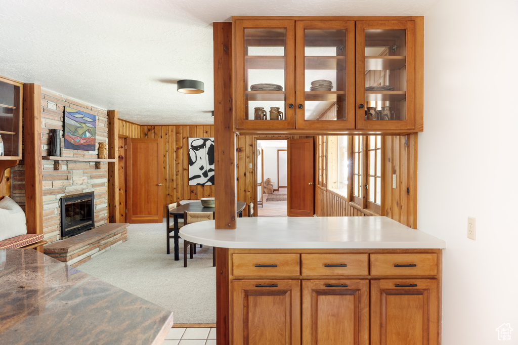 Kitchen featuring glass insert cabinets, a fireplace, wooden walls, light countertops, and brown cabinetry