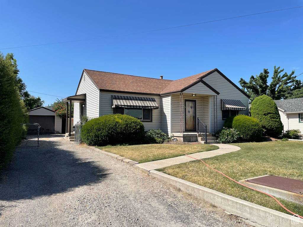 View of front of property featuring a front lawn, a shingled roof, an outbuilding, and gravel driveway