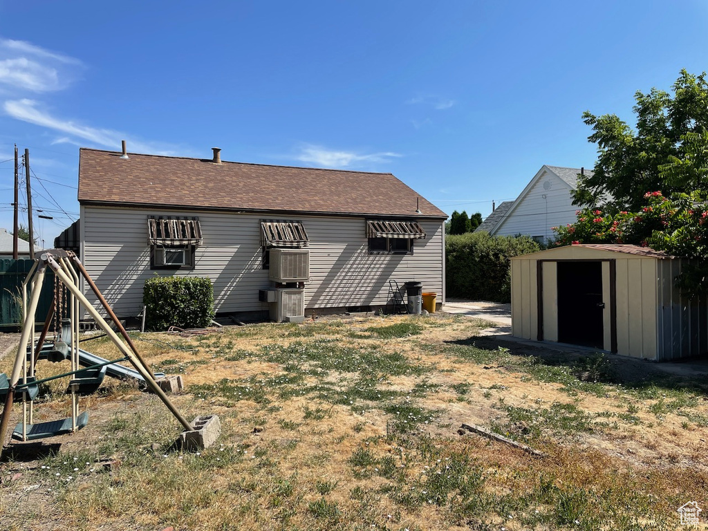 Back of property featuring a storage shed and a shingled roof