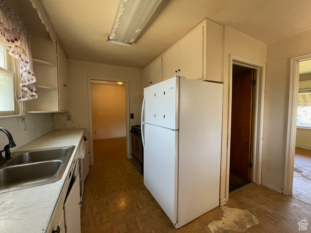 Kitchen with freestanding refrigerator, white cabinets, range, light countertops, and parquet flooring