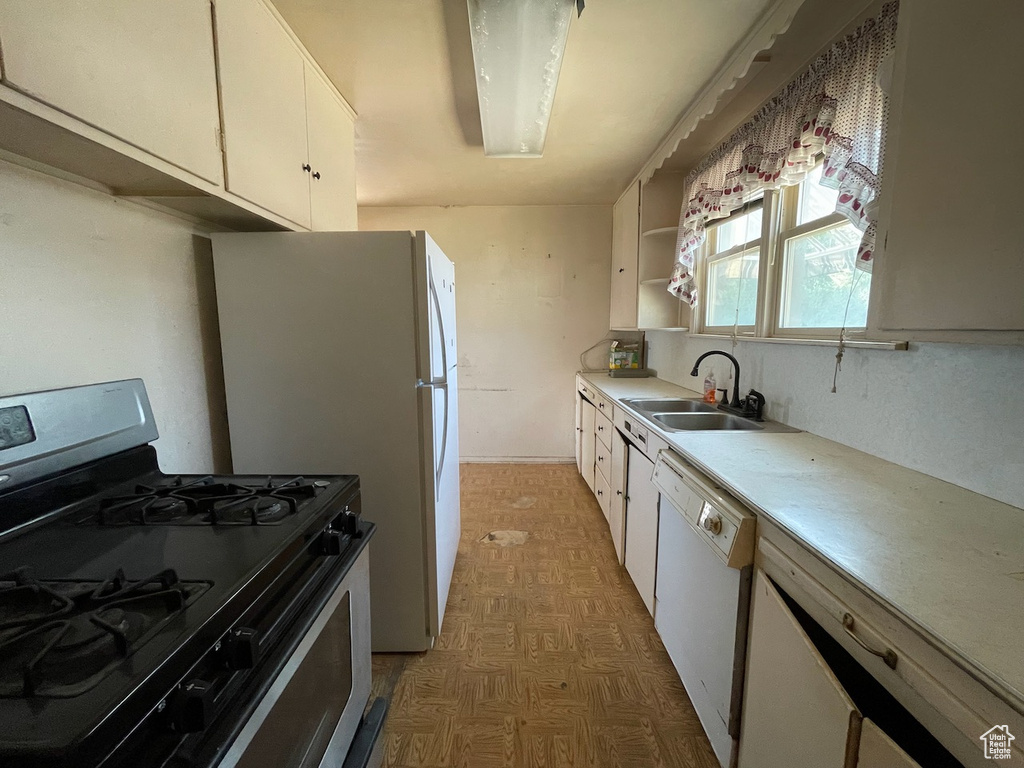 Kitchen featuring gas range, white dishwasher, light flooring, light countertops, and white cabinetry