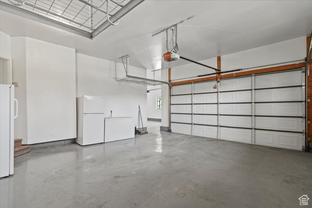 Garage featuring freestanding refrigerator, a garage door opener, and refrigerator