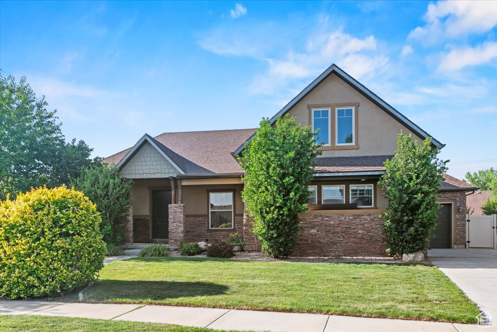 View of front facade featuring stucco siding, driveway, stone siding, and a front lawn
