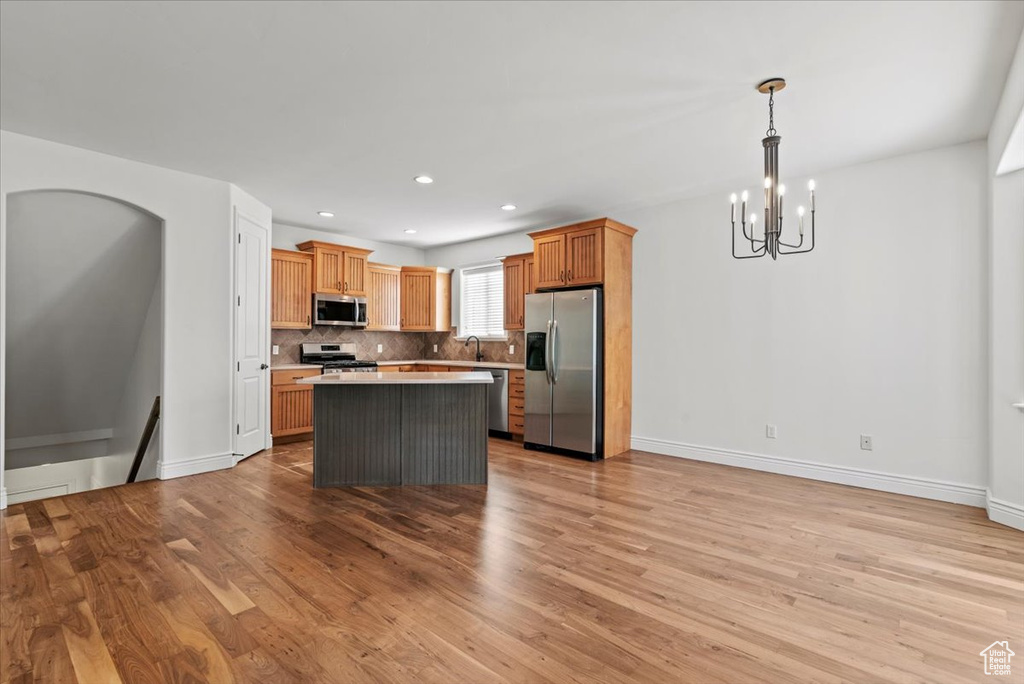 Kitchen with stainless steel appliances, a chandelier, light wood-style flooring, a kitchen island, and decorative backsplash