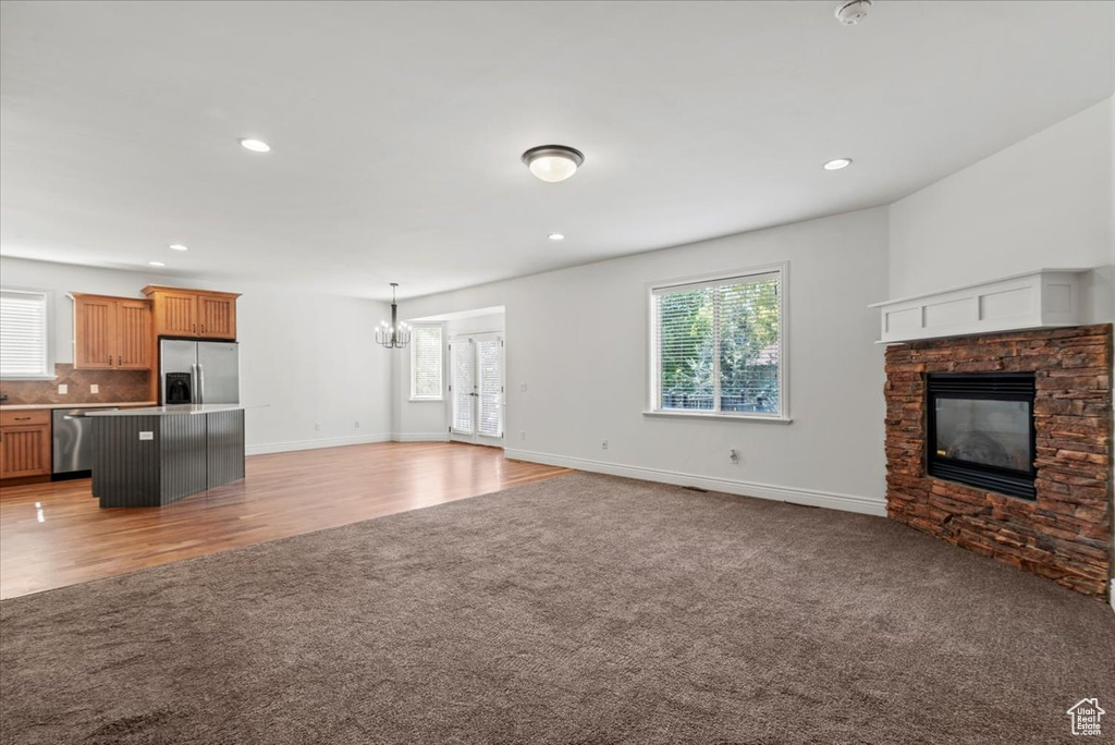 Unfurnished living room featuring light carpet, a fireplace, plenty of natural light, a chandelier, and recessed lighting