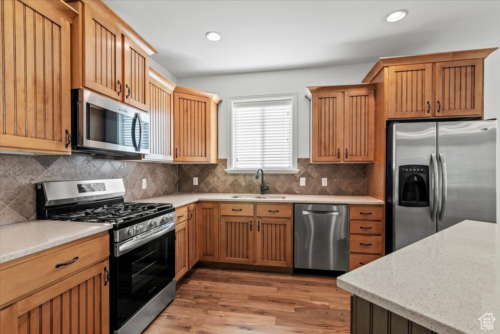 Kitchen with appliances with stainless steel finishes, light wood finished floors, tasteful backsplash, light stone countertops, and recessed lighting