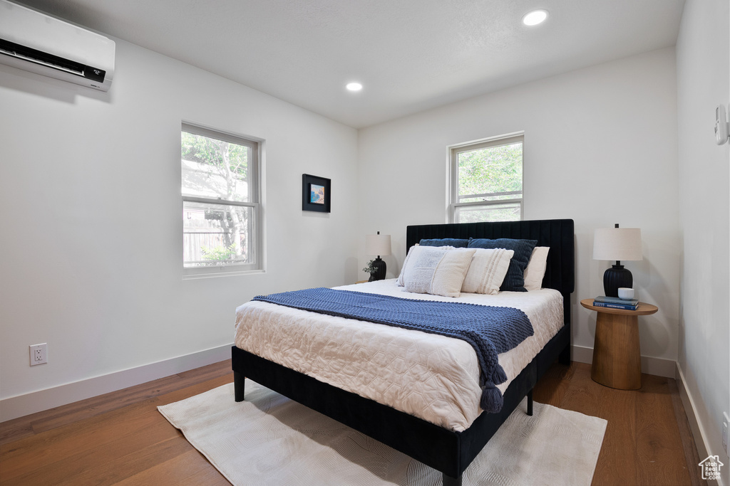 Bedroom with a wall mounted air conditioner, wood finished floors, and recessed lighting