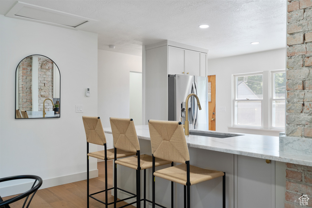 Kitchen featuring light wood-style flooring, stainless steel refrigerator with ice dispenser, light stone counters, a breakfast bar, and a textured ceiling