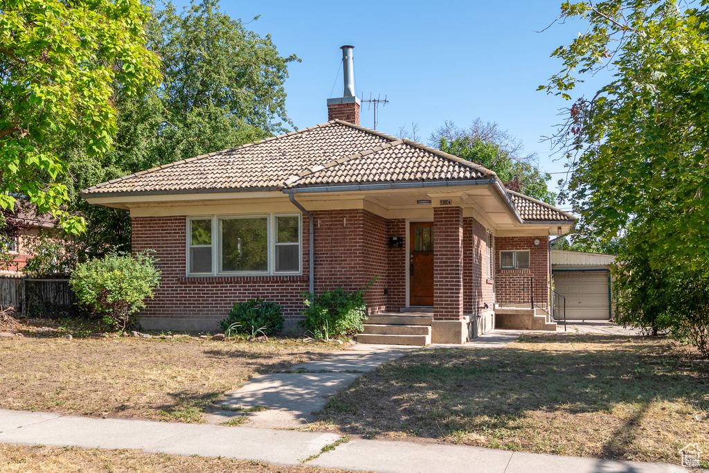 Bungalow-style home featuring brick siding, a chimney, a tile roof, and a garage