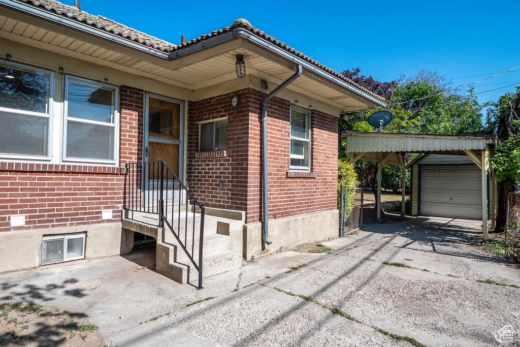 Doorway to property featuring brick siding, asphalt driveway, a garage, and a carport