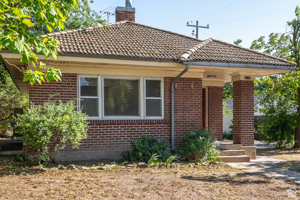 View of front of home with brick siding, a tiled roof, and a chimney