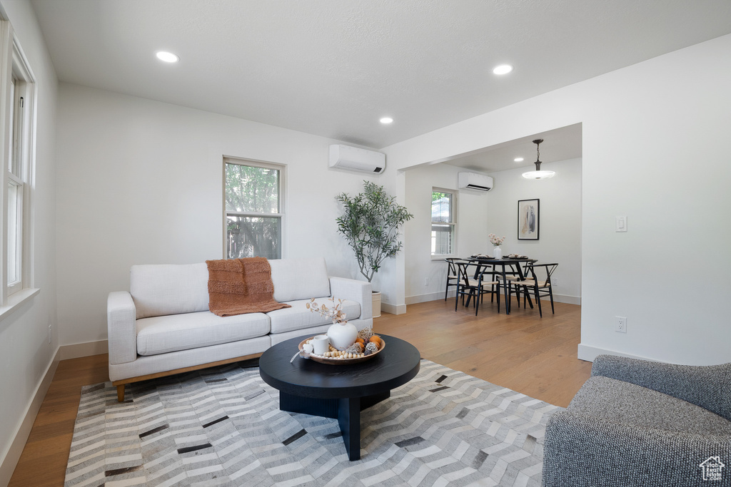 Living area featuring an AC wall unit, light wood-type flooring, and recessed lighting