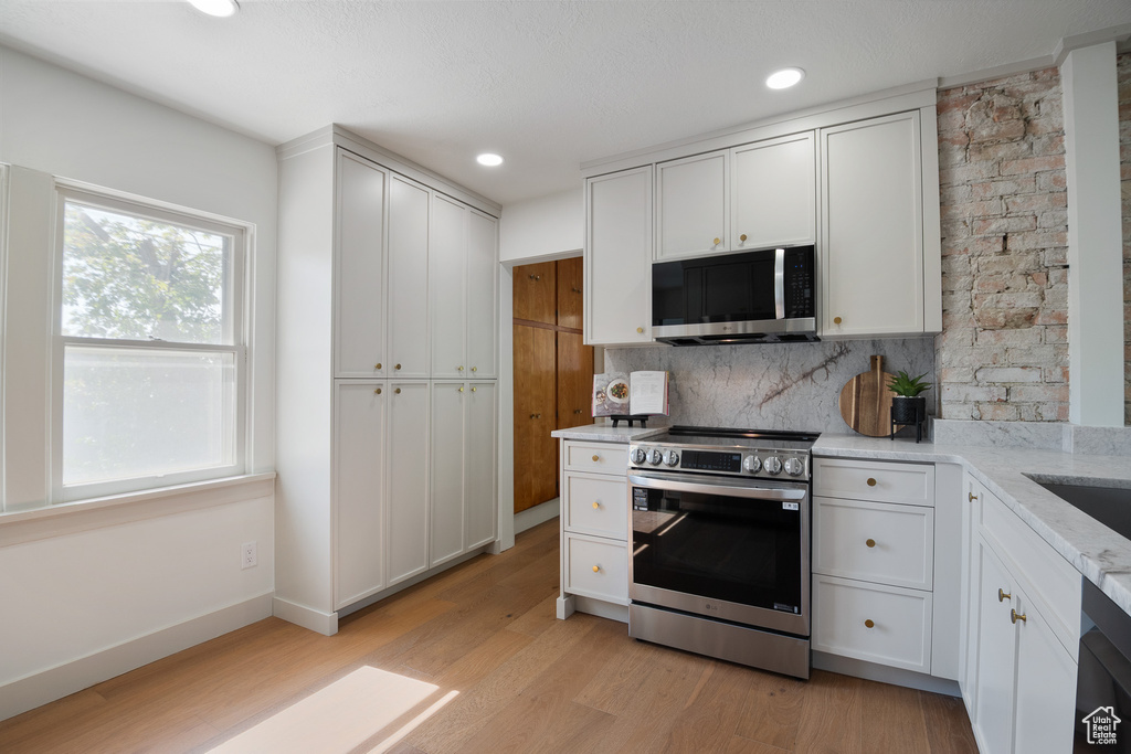 Kitchen with appliances with stainless steel finishes, decorative backsplash, light wood finished floors, white cabinets, and recessed lighting