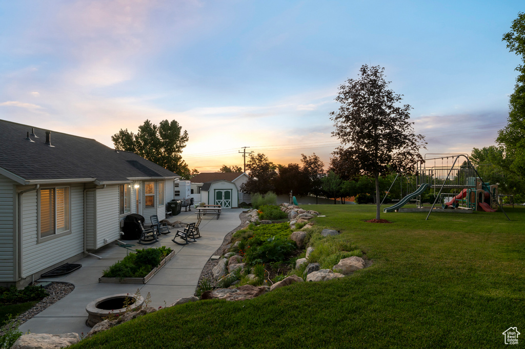 Yard at dusk with a patio area, a yard, a playground, and an outbuilding