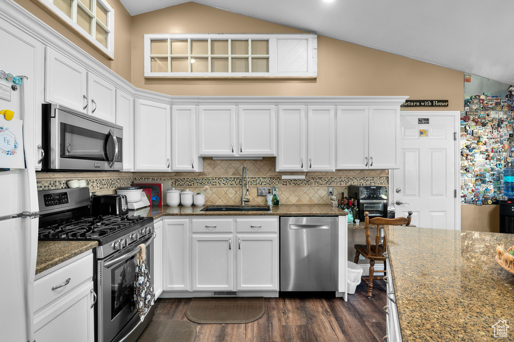Kitchen featuring appliances with stainless steel finishes, lofted ceiling, white cabinets, dark wood-style floors, and dark stone counters
