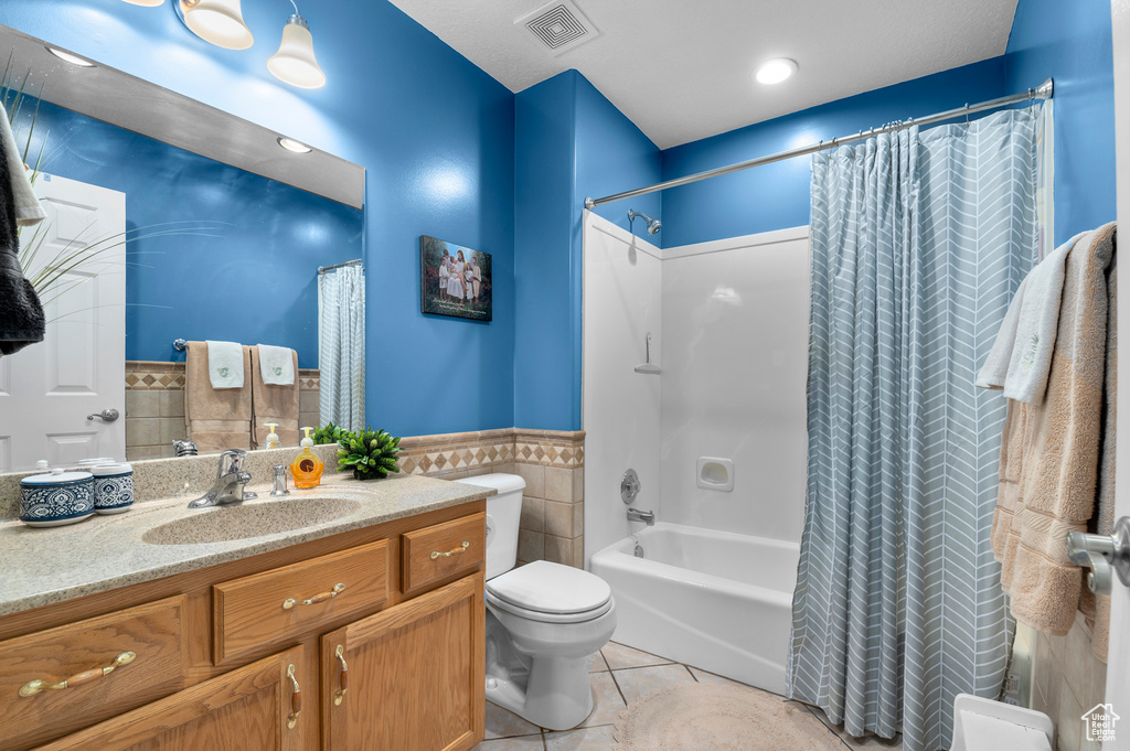 Full bathroom featuring tile walls, vanity, shower / tub combo, tile patterned floors, and a wainscoted wall