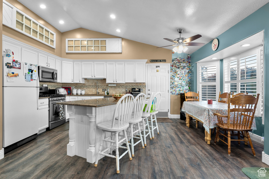 Kitchen with stainless steel appliances, vaulted ceiling, a kitchen bar, white cabinetry, and a ceiling fan