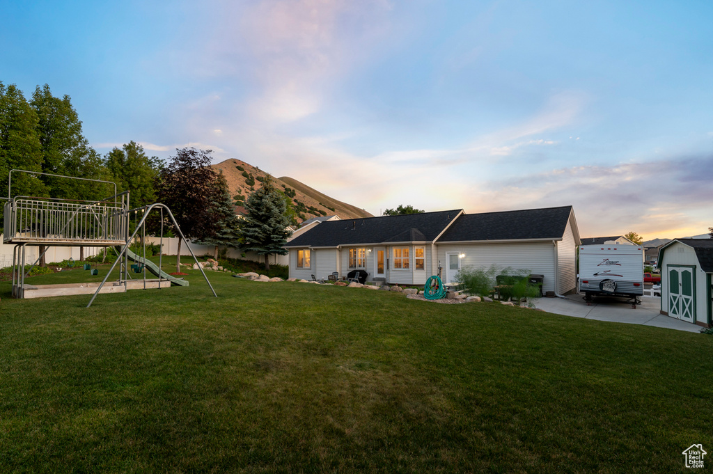 Back of house at dusk featuring a yard, a storage unit, a playground, and a patio area