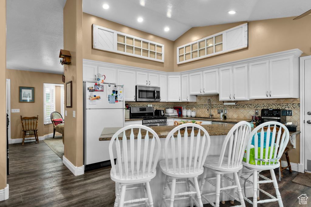Kitchen with stainless steel appliances, white cabinetry, decorative backsplash, a kitchen breakfast bar, and high vaulted ceiling