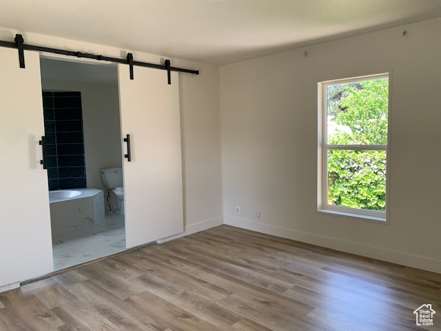 Unfurnished bedroom with a barn door, wood finished floors, and connected bathroom