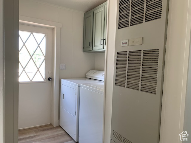 Laundry area with a heating unit, cabinet space, separate washer and dryer, and light wood-style floors