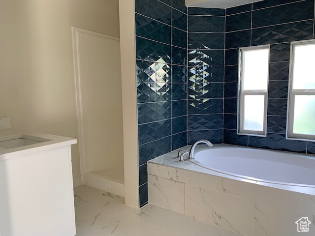 Bathroom with marble look tiles, a bath, vanity, and a walk in shower