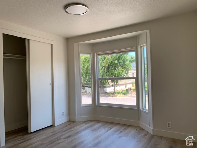 Unfurnished bedroom featuring wood finished floors, a textured ceiling, multiple windows, and a closet