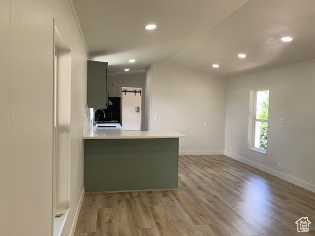 Kitchen featuring light wood-type flooring, light countertops, ornamental molding, recessed lighting, and a peninsula