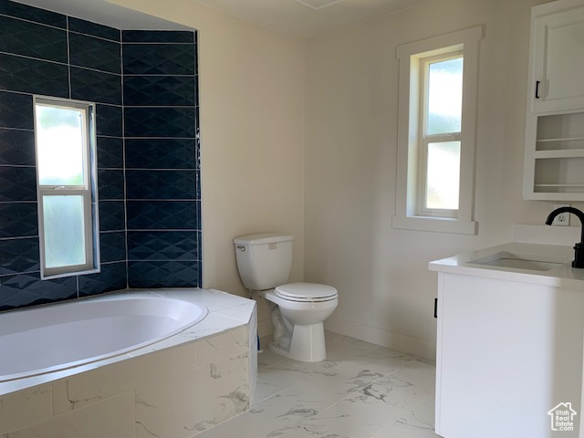 Bathroom featuring marble look tile flooring, vanity, and tiled bath