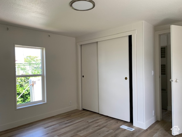 Unfurnished bedroom with light wood-style floors, multiple windows, and a closet