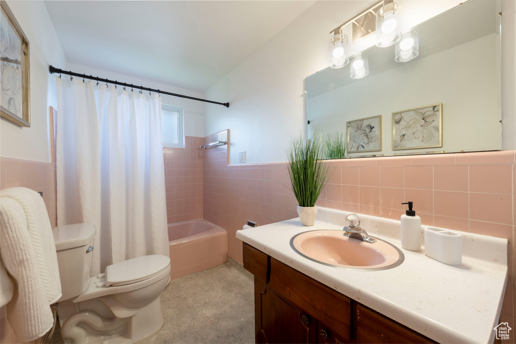 Bathroom with tile walls, vanity, shower / bath combo with shower curtain, and wainscoting